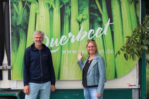 Thomas Wolff, Geschäftsführer von Querbeet, mit Erster Kreisbeigeordneter Stephanie Becker-Bösch, stehend vor Fahrzeug mit großflächiger Querbeet Werbung mit Staudensellerie als Motiv