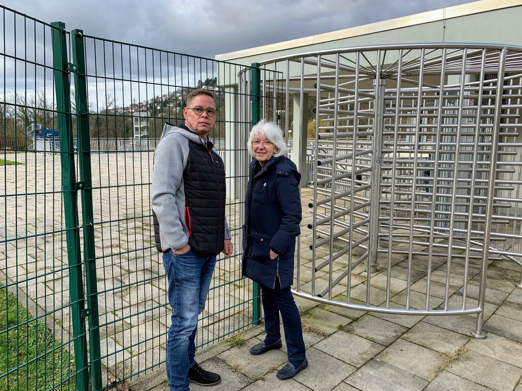 Manfred Scheid-Varisco und Sieglinde Huxhorn-Engler vor Drehkreuz und hohem Zaun am Eingang des Büdinger Schwimmbads